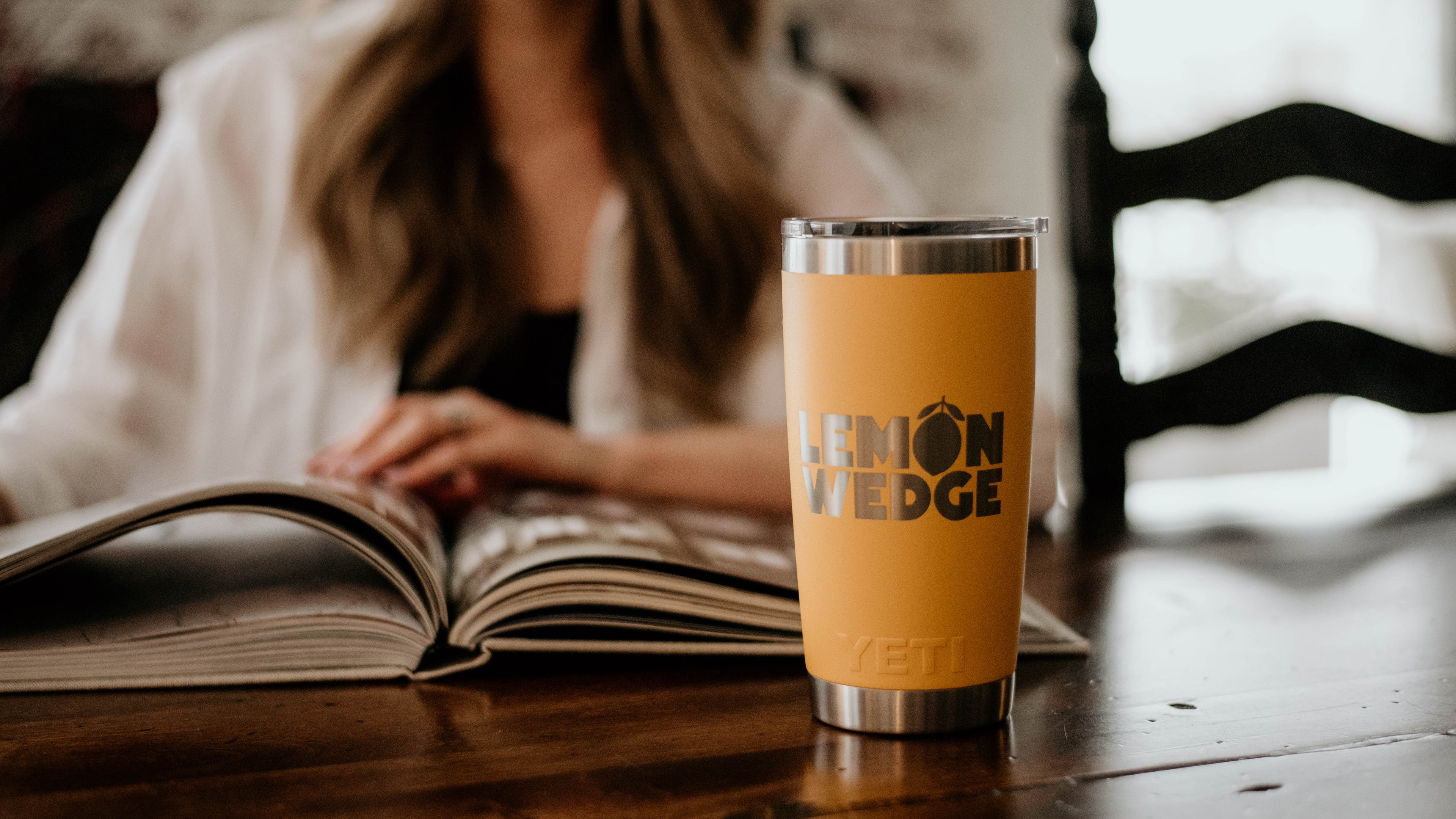Yellow tumbler with 'Lemon wedge' logo on a wooden table next to an open book.